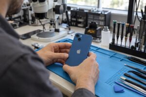 Mavi iPhone 13 modelinin çapraz çift arka kamerasıyla atölyede incelenmesini gösteren temsili sahne